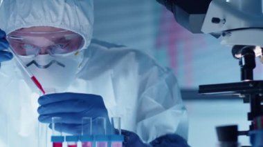 Koruyucu üniformalı bir erkek bilim adamının laboratuarda antiviral tedavi üzerine tıbbi araştırmalar yaparken pipetten tüpe kan dökerken görüntüsü.