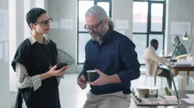 Mimarlık ofisinde kahve molası verirken üst düzey bir erkek arkadaşla akıllı telefondan konuşan orta yaşlı bir iş kadını.