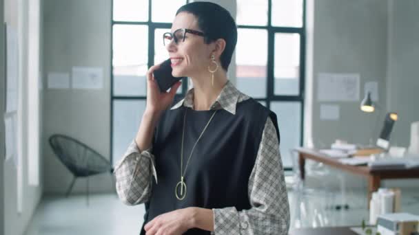 美しい中世の実業家女性とともに短いブルネットの髪立ってオフィスでと仕事中に携帯電話で話す — ストック動画
