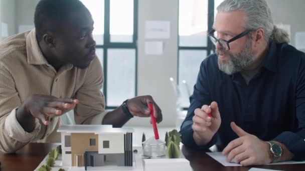 若いアフリカ系アメリカ人男性は オフィスで建築プロジェクトを共同作業しながら シニア男性同僚と建築モデルを議論 — ストック動画