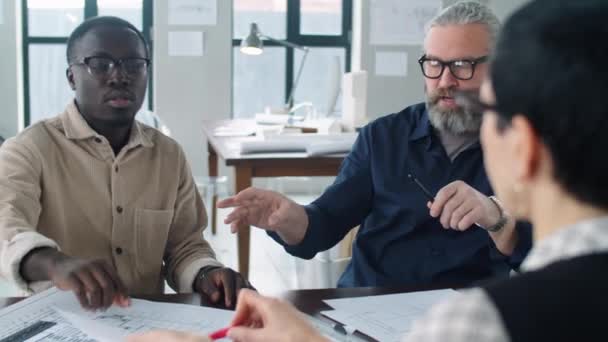 若いアフリカ系アメリカ人建築家と彼の同僚の肩のショットの上にオフィスミーティング中に女性の上司と紙の上のフロアプランを議論 — ストック動画