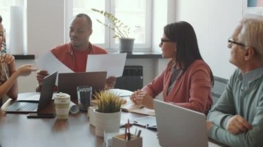 Genç Afro-Amerikan yöneticinin PAN karesi dokümanları kontrol ederken ve çeşitli yaş gruplarıyla iş fikirlerini tartışırken ofis toplantılarında birlikte çalışırken.