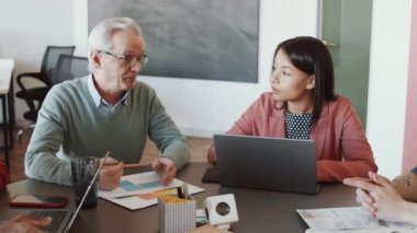 Gözlüklü ve günlük kıyafetlerle üst düzey Kafkasyalı bir adamın ofis toplantısı sırasında bir grup genç çoklu etnik kökenli iş arkadaşına iş fikrini açıklarken görüntüsü.