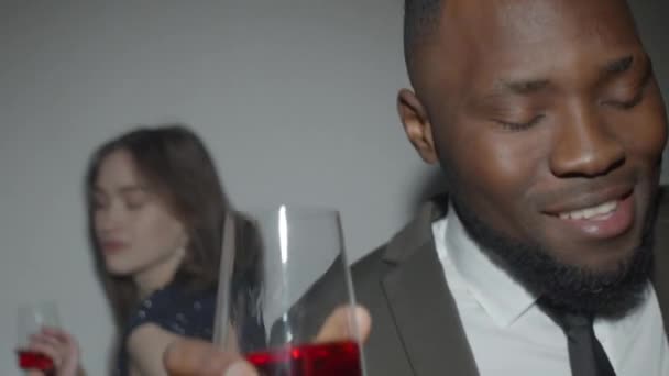 身穿时髦西服的年轻的喝醉的非洲裔美国男人举着酒杯 对着相机微笑 并在宴会上与白人女子共舞 — 图库视频影像