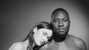 Stüdyoda kameraya birlikte poz verirken Afro-Amerikalı erkek arkadaşının omzuna yaslanan siyah-beyaz beyaz beyaz bir kadın portresi.