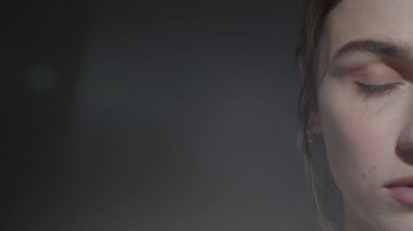 Makyajsız güzel bir genç kadının yüzünün yarısını kapayın. Sol tarafta fotokopi alanı olan karanlık bir arkaplanda kameraya poz verin.