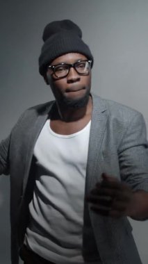 Moda kıyafetli, bereli ve dumanlı gözlüklü rahat Afro-Amerikan genç adamın dikey çekimleri.