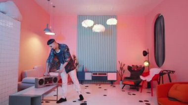 Genç şık bir adam yaratıcı bir şekilde tasarlanmış odaya giriyor, kaset çaları açıyor ve vogue dansı yapıyor.