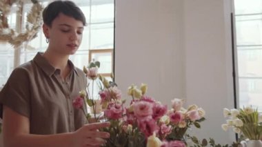 Kısa saçlı, güzel gülleri inceleyen, gülümseyen ve çiçekçide dijital tablet yazan güzel bir kadın.