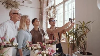 Bir grup neşeli, yaşlı kadın gülümseyen ve akıllı telefon kamerasına poz verirken çiçekçi erkek çiçekçi çiçekçi atölyesindeki çiçekçiden sonra selfie çekiyor.