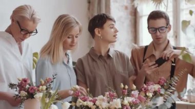 Önlüklü genç bir erkek çiçekçi, çiçekçide çalışırken akıllı telefon kamerasına gülümsüyor ve poz veriyor.