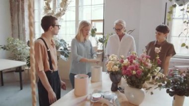Profesyonel kadın çiçekçi atölyede yüksek lisans yaparken şapka kutusunda genç bir adam ve iki kadına çiçek kompozisyonu yapmayı anlatıyor.