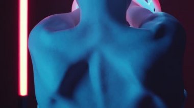 Arkadan bakıldığında, kel kafalı, parlak neon tüplü, floresan lambalı ve karanlık stüdyoda duran bir kadının görüntüsü var.