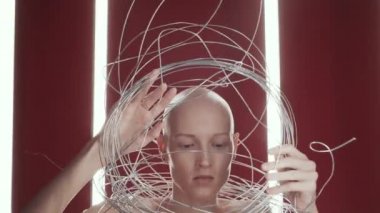 Stüdyodaki çıplak kel kadın modelinin dikey floresan lambalı koyu kırmızı arka planda durduğu sahneyi çekelim.