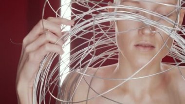 Stüdyoda dikey floresan lambalarla birbirine dolanmış bir şekilde kameraya bakarken kazıksız genç bir kadının görüntüsünü kaldır.