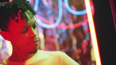 Disko topu tutan, gülümseyen ve dans eden, yanıp sönen neon ışıkları ve arka planda parlayan tüpleri olan genç, Afro-Amerikan adamın göğüs yukarı çekimi.