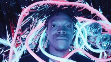 Parlak neon tüpleri ve disko toplarıyla metalik folyo üzerinde uzanmış, kameraya bakıp gülümseyen genç, yakışıklı Afrikalı Amerikalı 'nın en iyi görüntüsü.