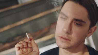 İpek bornozlu yakışıklı bir transseksüelin, başını duvara yasladığı, alkol aldığı, sigara içtiği ve kameraya baktığı yakın çekim.