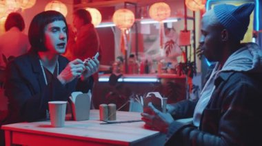 Cinsiyet değiştiren adam, Çin restoranında masada oturup yemek yerken ruj sürüyor ve Afro-Amerikan erkek arkadaşıyla konuşuyor.