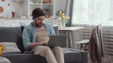 Sakallı adam koltukta oturup dizüstü bilgisayar kullanırken neşeli karısı ona yastıkla vuruyor ve gülüyor, sonra da heyecanlı çift oturma odasında yastık savaşı yapıyor.