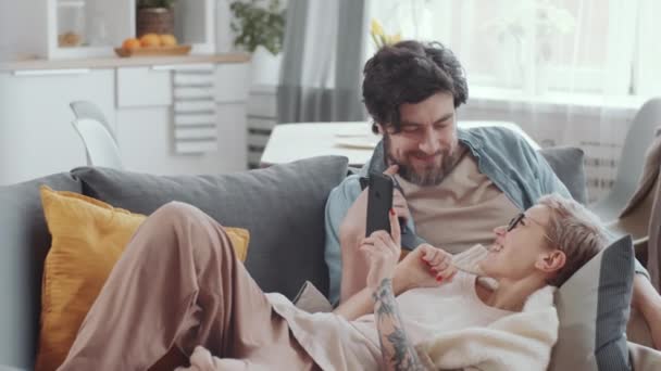 Genç Karı Kocanın Internette Akıllı Telefonlarla Gezinip Evdeki Kanepede Dinlenirken — Stok video