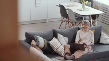 Kafkasyalı kadının elinde kredi kartı ve dizüstü bilgisayarla evde karantinada internet üzerinden alışveriş yaparken yüksek açılı görüntüsü.