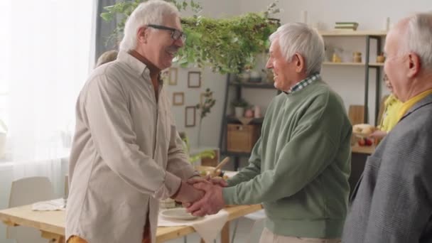 Senioren Mannelijke Vrienden Glimlachen Praten Handen Schudden Thuis Partij Terwijl — Stockvideo