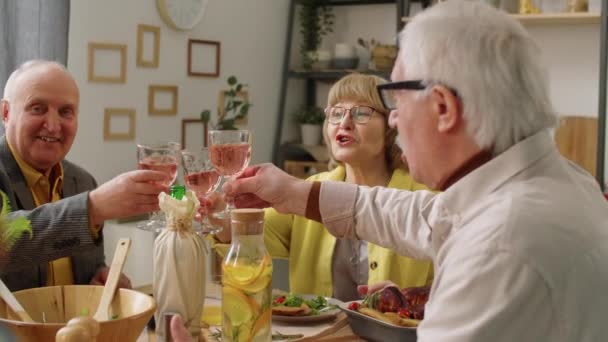 上了年纪的朋友们一边坐在餐桌前 一边在庆祝自己的家 一边笑着 并在敬酒的时候碰碰酒杯 — 图库视频影像