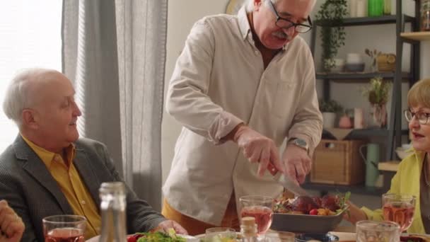 老人はローストチキンを切断し 家庭のディナーでゲストのためのプレート上に肉の一片を置く — ストック動画