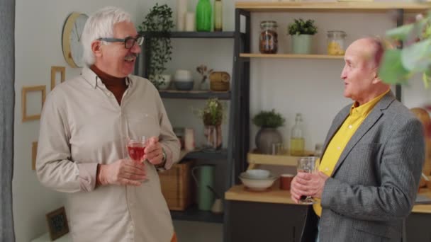 ワインのグラスを持って立っている2人の上級男性の友人 笑顔と自宅パーティーで話す — ストック動画