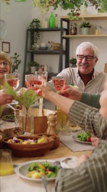 Mutlu kıdemli arkadaşlardan oluşan dikey bir çekim. Evde Noel yemeği yerken kadeh tokuşturuyorlar.