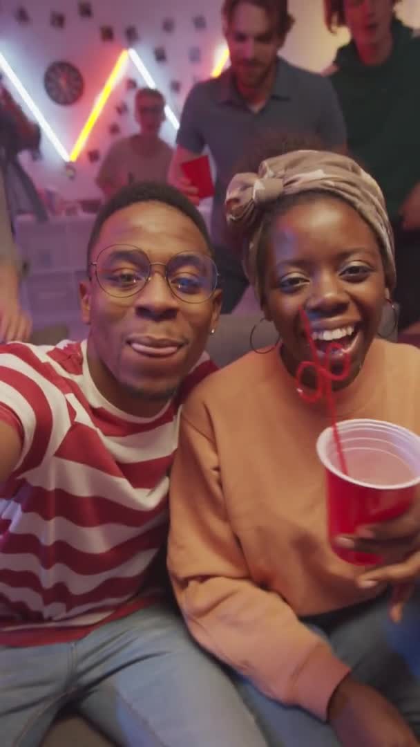 明るい友人がそれらに参加しながら 若いアフリカ系アメリカ人のカップルの垂直ショットは ホームパーティーで自画自身を取ります 笑顔とカメラのために一緒にポーズ — ストック動画