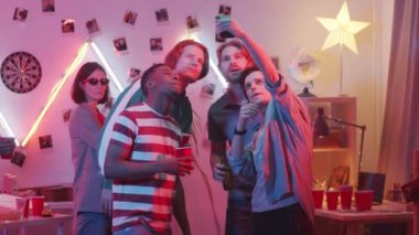 İçki içen, gülümseyen ve birlikte poz veren bir grup genç adam, partideki akıllı telefonlu kız arkadaşlarıyla selfie çekiyorlar, sonra da fotoğraf çekinip gülüyorlar.