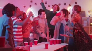 Kırmızı plastik bardaktan içen neşeli genç bir kadın bira pong maçını kaybederken, etnik çeşitliliğe sahip arkadaşları da ev partisinde ona tezahürat yapıyor.