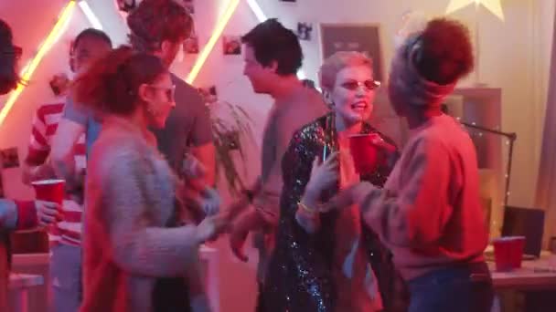 在家里的派对上 穿着时髦的年轻女性一边喝酒一边聊天和大笑 一边在有霓虹灯的房间里与男性朋友共舞 — 图库视频影像