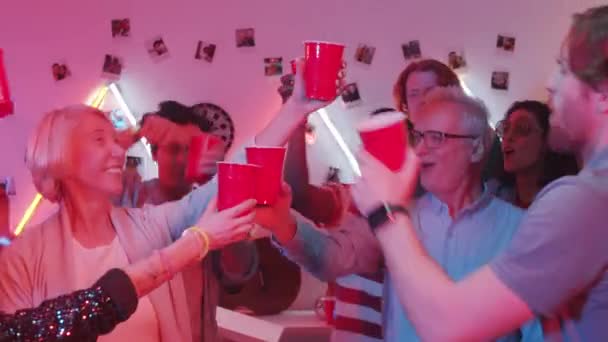 喜びの多民族の友人の混合高齢者のグループは ダンス 笑顔と色ネオンと部屋のパーティーで赤いプラスチックカップで乾杯 — ストック動画