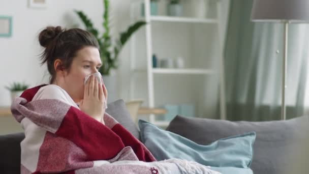 在家里的沙发上 用毯子包裹着不健康的年轻女子的照片 用餐巾纸吹鼻涕 然后在感染流感时检查医疗温度计 — 图库视频影像