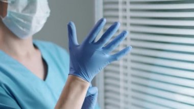 Steril şapkalı, maskeli ve üniformalı kadın doktor koruyucu eldiven takıyor ve iş günü hastanede yürüyüp gidiyor.