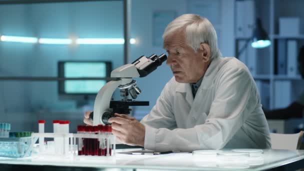 Ανώτερος Καυκάσιος Επιστήμονας Εργαστηριακή Ποδιά Κάθεται Στο Γραφείο Στο Εργαστήριο — Αρχείο Βίντεο