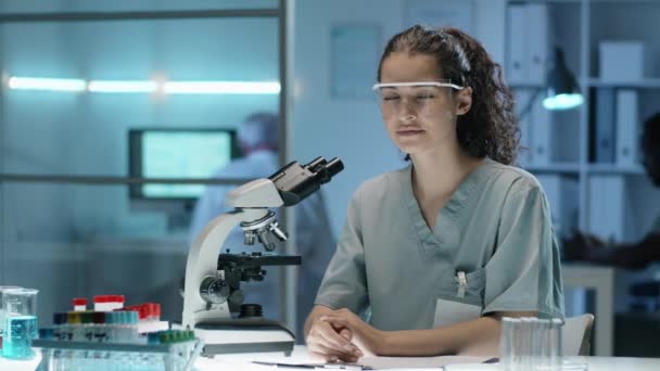 Retrato Jovem Bela Cientista Uniforme Óculos Sentados Mesa Laboratório Olhando — Vídeo de Stock