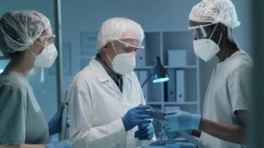 Koruyucu üniformalı kıdemli bilim adamı, Covid salgını sırasında laboratuvarda birlikte çalışırken çok ırklı genç meslektaşlarına panolardaki bir şeyi açıklıyor.