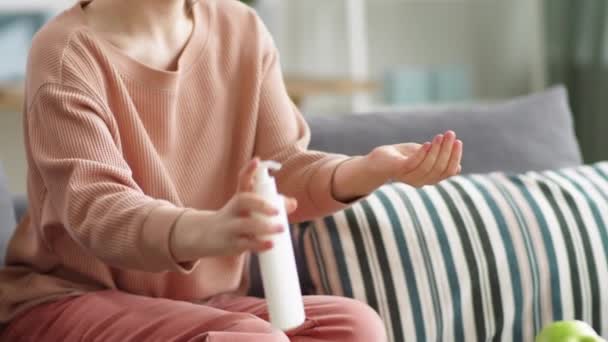 年轻女人用清洁剂擦拭双手 然后在家里坐在沙发上使用智能手机 Covid 19预防概念 — 图库视频影像