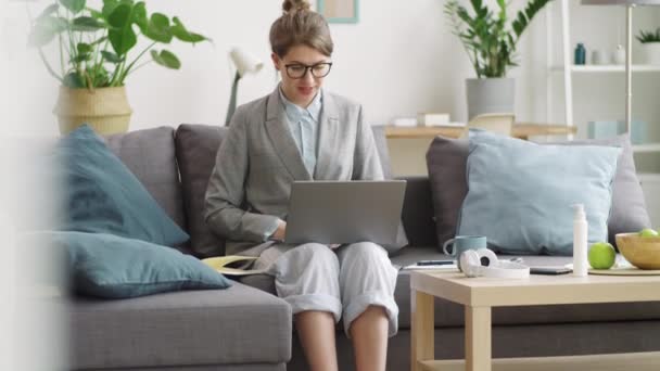穿着毛绒绒拖鞋 正式衬衫和运动衫的女商人坐在家里沙发上 孤零零地坐在笔记本电脑上举行远程会议 给出财务图表的照片 — 图库视频影像