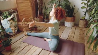 Spor giyimli, genç ve esnek bir kadının evdeki yoga antrenmanı sırasında baş-diz öne eğip antrenman yapmasını yakınlaştır.