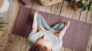 Spor kıyafetleri içinde çıplak ayaklı bir kadının Lotus 'ta poz verirken ve evde yoga yaparken çamurda el ele tutuşurken.