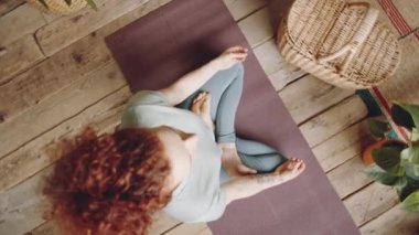 Üst görüntüde çıplak ayaklı, kıvırcık saçlı, nilüferde poz veren, çamurda el ele tutuşan ve evde ahşap zemin ile yoga meditasyonu yapan bir kadın var.