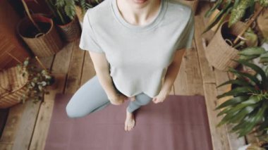 Kadının ağaçta durduğu yüksek açı pozu ve evinde yoga yaparken göğsünün önünde dua pozisyonunda el ele tutuşması.