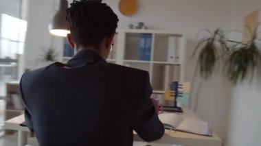 Gözlüklü genç Afro-Amerikan iş adamının 360 derecelik izleme görüntüsü ofisteki bilgisayarında çalışırken arka planda çalışan bayan meslektaşı...