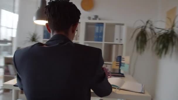 彼の女性の同僚がバックグラウンドで作業しながら オフィスの机の上でノートパソコン上で作業眼鏡で若いアフリカ系アメリカ人ビジネスマンの360度の追跡ショット — ストック動画
