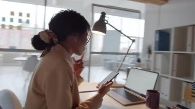 Ofis masasında erkek arkadaşı bilgisayarla arka planda çalışırken Afro-Amerikan iş kadınının gülümseyip mesaj attığı 360 derecelik bir izleme görüntüsü.